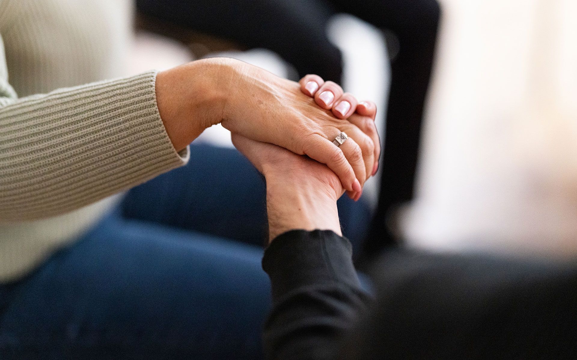 A woman is holding another woman 's hand while sitting on a couch.