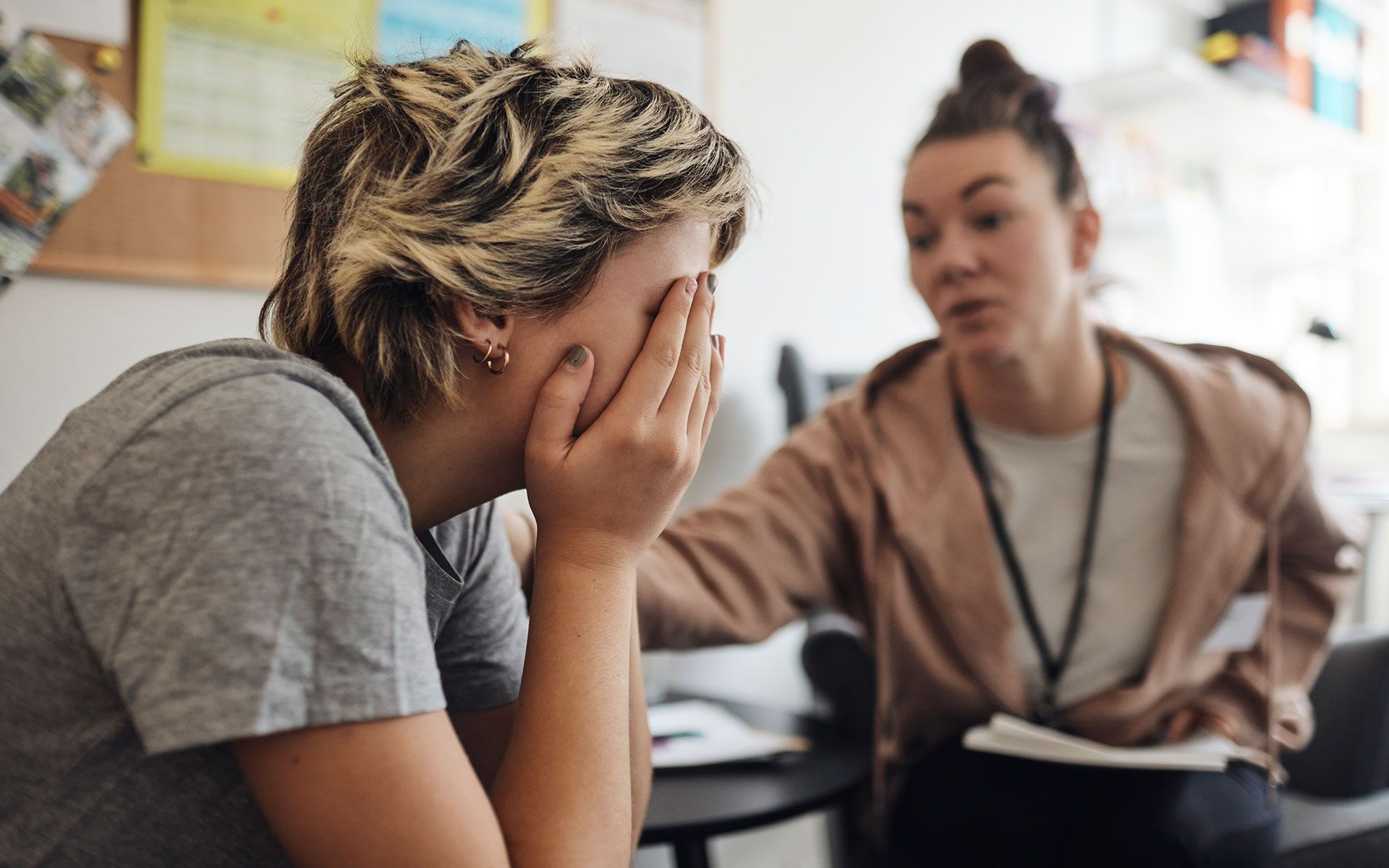 A woman is covering her face while talking to another woman.
