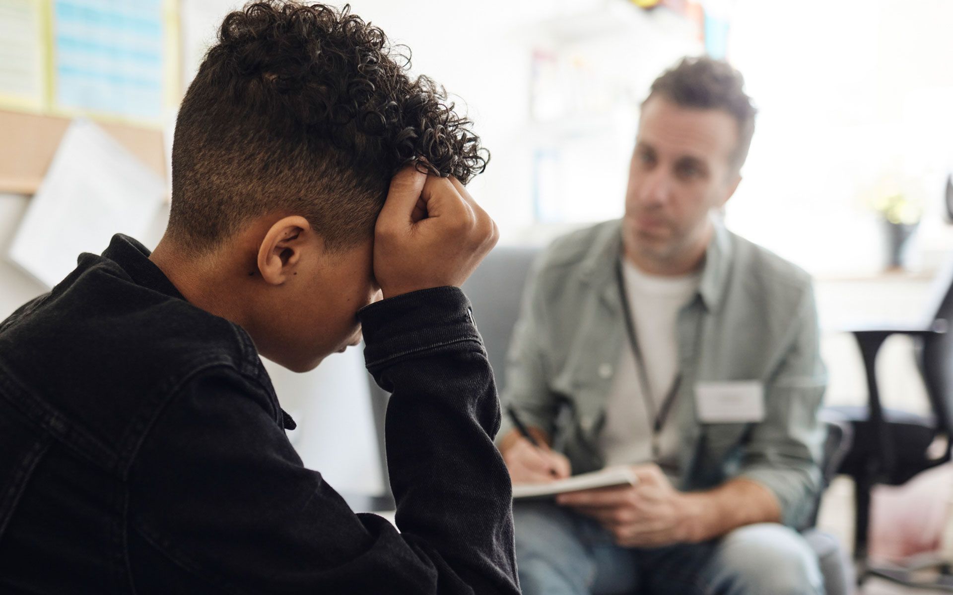 A man is talking to a young man who is sitting on a couch.