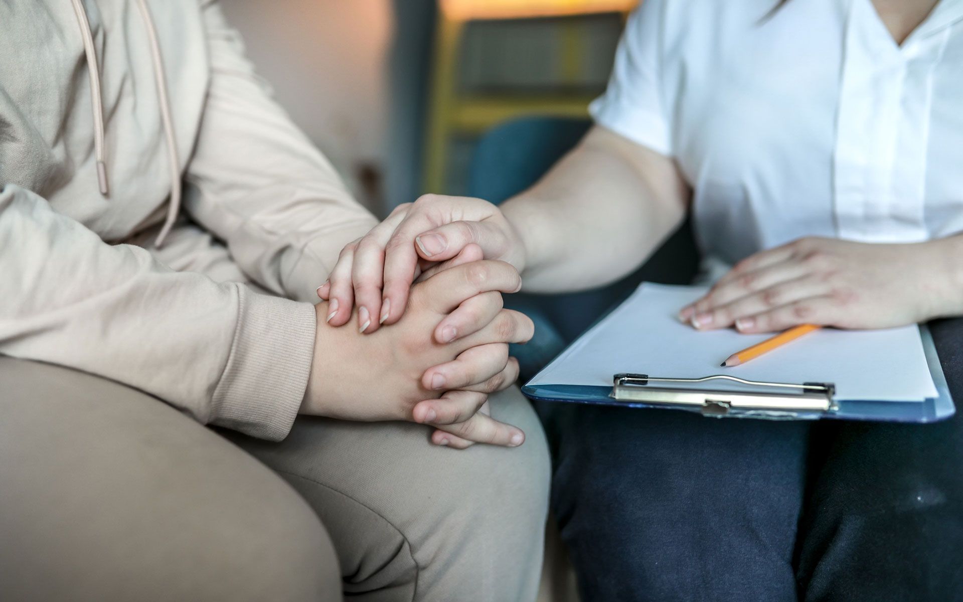 A woman is holding another woman 's hand while sitting on a couch.