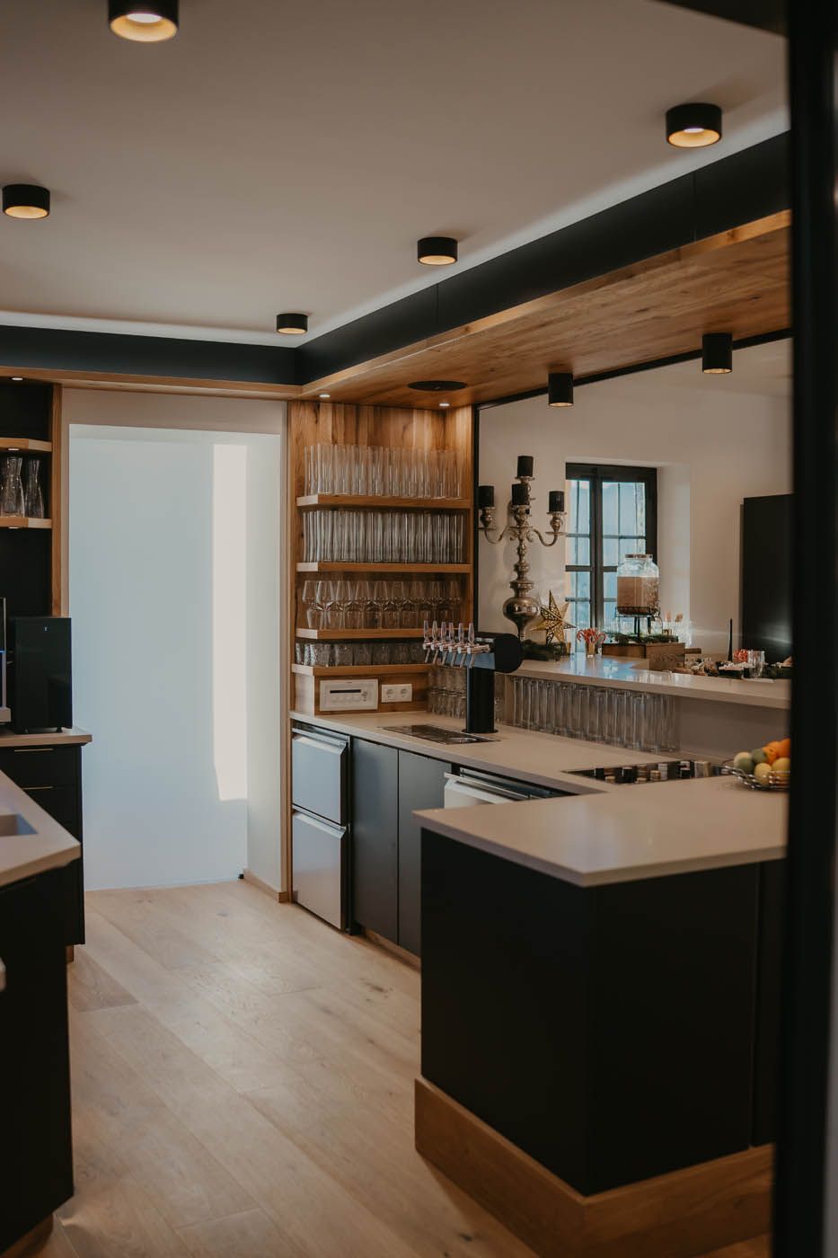Moderne Küche mit Holzelementen, schwarzen Schränken, Edelstahlgeräten und Deckenbeleuchtung.