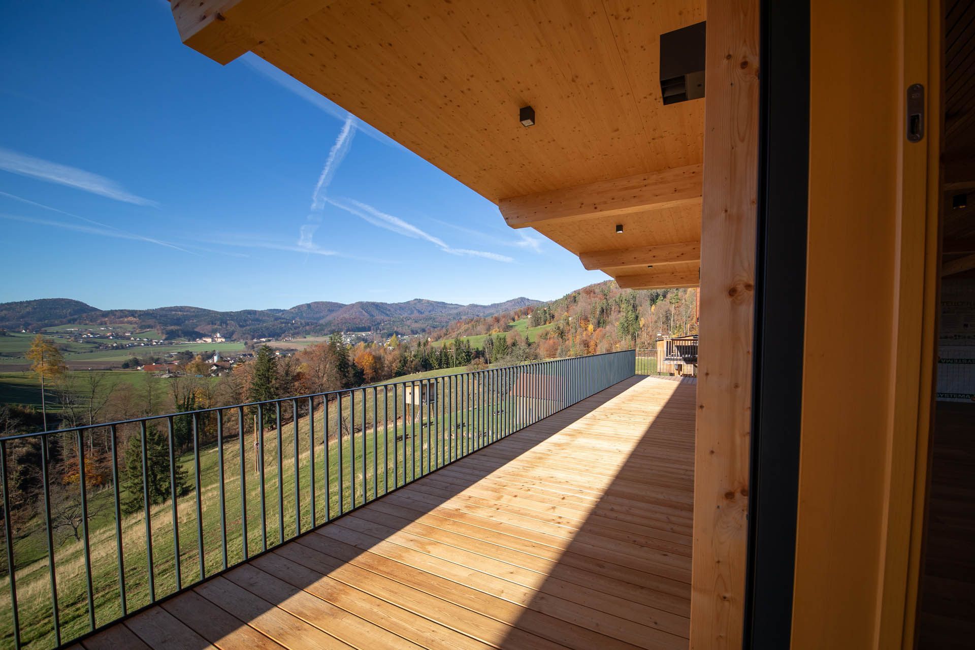 Ein hölzerner Balkon mit Blick auf eine ländliche Landschaft mit Bergen und klarem blauen Himmel.