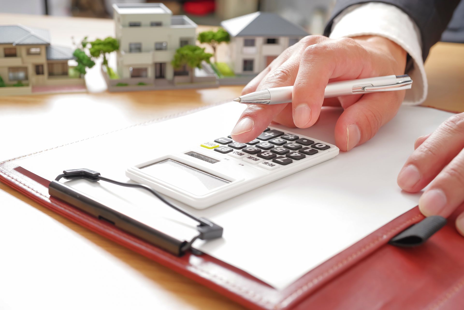 Financial advisor calculating rates with a calculator and house models for a collateral loan.