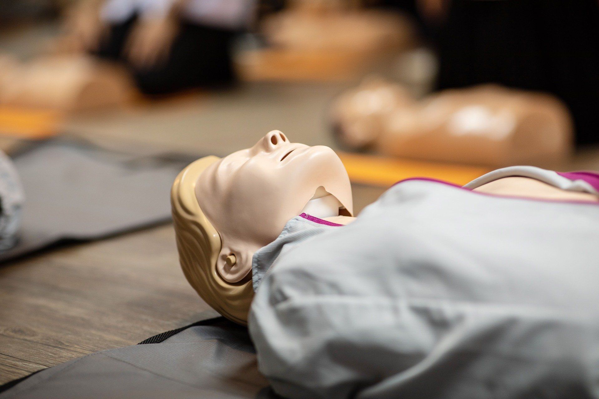 CPR training dummy lying on a mat, mouth open, in a classroom setting.