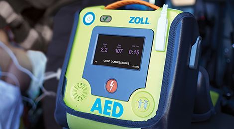 AED device with screen displaying data, sitting in a vehicle. Yellow, blue, and black colors.