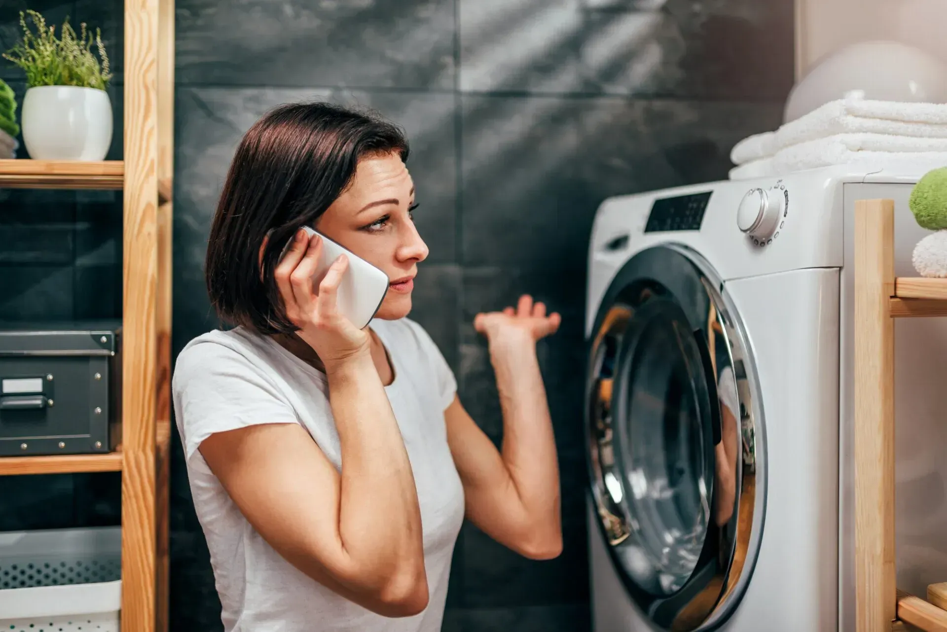 Woman talking on a phone beside a front-loading washing machine in a laundry room