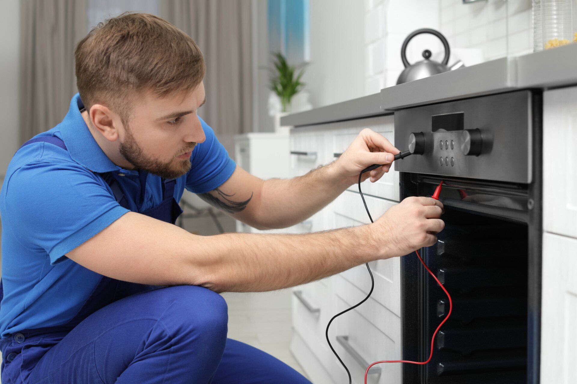 Technician in blue uniform adjusting wiring on a black appliance in a bright kitchen.
