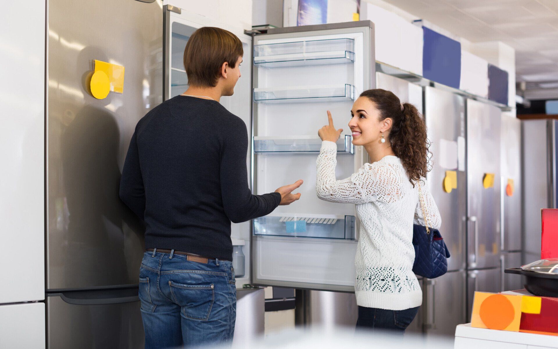 Two people in a kitchen opening a refrigerator and examining the shelves