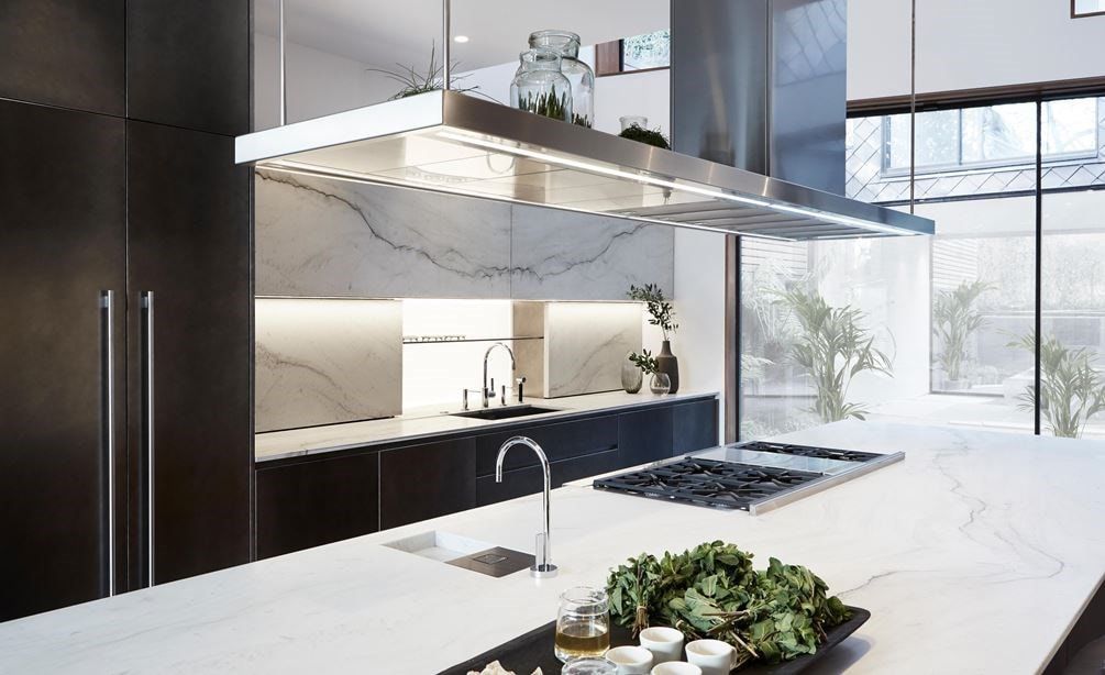 Modern kitchen with white island, stainless hood, cooktop, and large window view