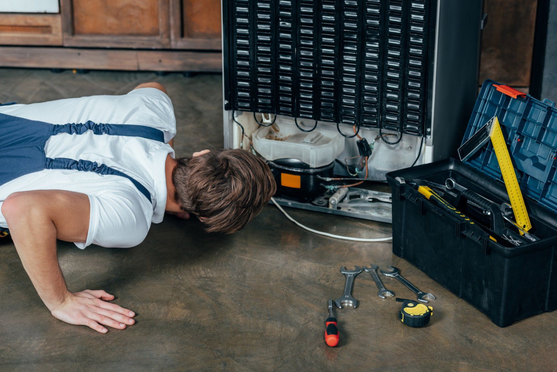 a man is laying on the floor fixing a refrigerator .