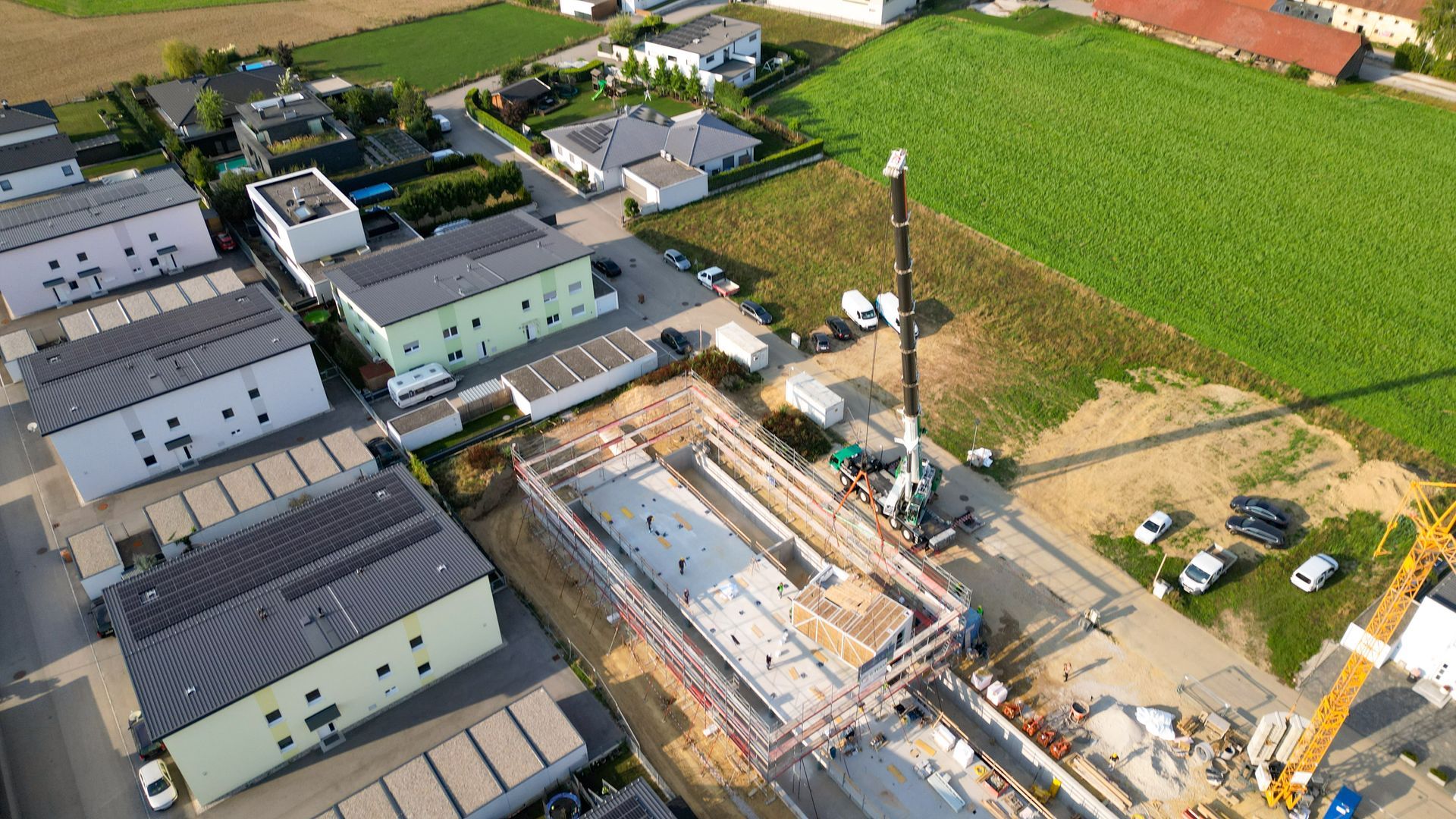 Luftaufnahme einer Baustelle mit Kran, Häusern und Feld.