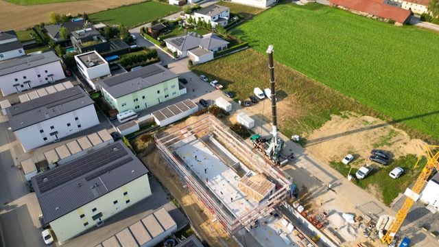 Luftaufnahme einer Baustelle mit einem Kran, umgeben von Gebäuden und einem Feld.