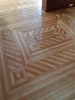 Parquet en bois à motifs géométriques dans une pièce, avec des tons de bois clairs et foncés.