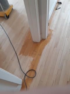 Parquet taché d'eau autour d'une porte, avec un câble qui traîne sur le sol.