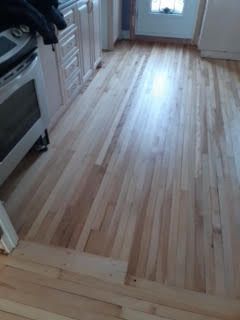 Sol de cuisine en bois clair avec placards et cuisinière sur le côté gauche, éclairée par la lumière du soleil près de la porte arrière.