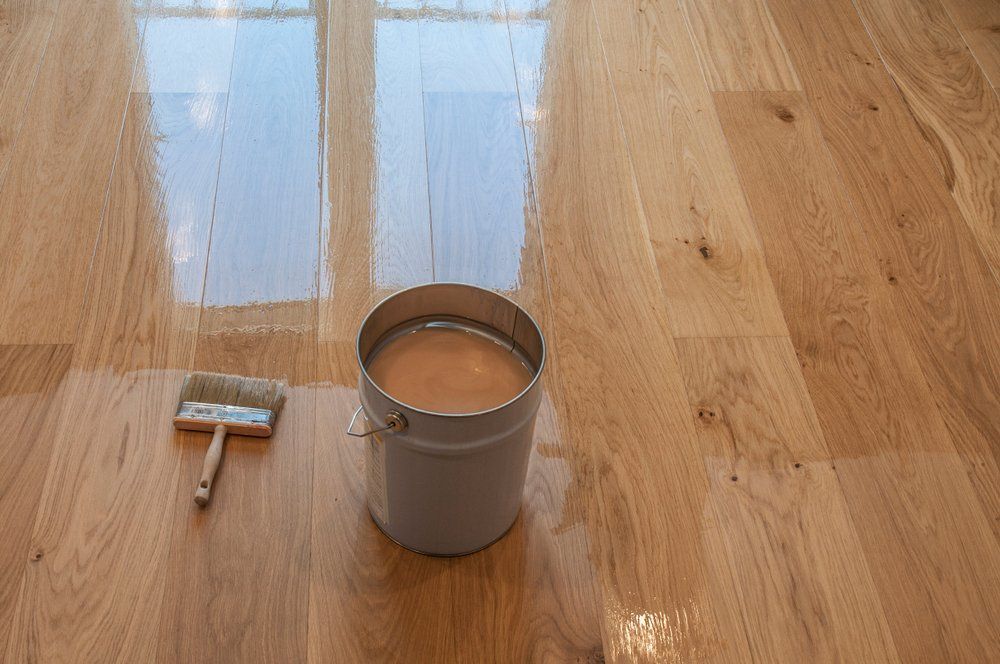 Pot de peinture et rouleau à peinture sur un parquet brillant près d'un vernis à base d'eau fraîchement appliqué