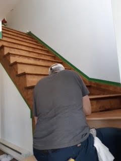 Une personne accroupie sur un escalier en bois, en train de peindre les moulures murales en vert.