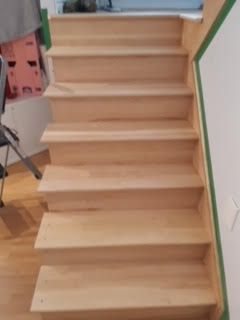Escalier intérieur en bois clair avec marches non finies et ruban adhésif vert le long du mur de droite