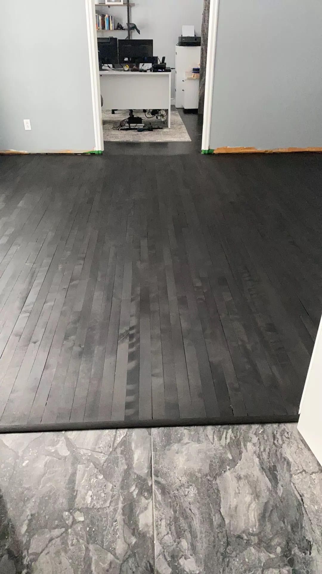 Sol en bois foncé dans une pièce vide, avec un petit tapis au bas de la pièce et une porte au fond.