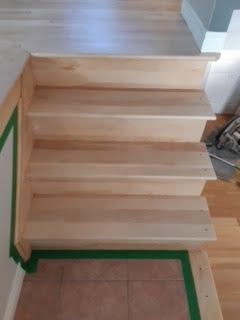 Escalier en bois avec du ruban adhésif vert sur les bords, menant d'un sol carrelé.
