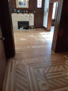 Salon vide avec parquet à motifs et cheminée, vu à travers une porte