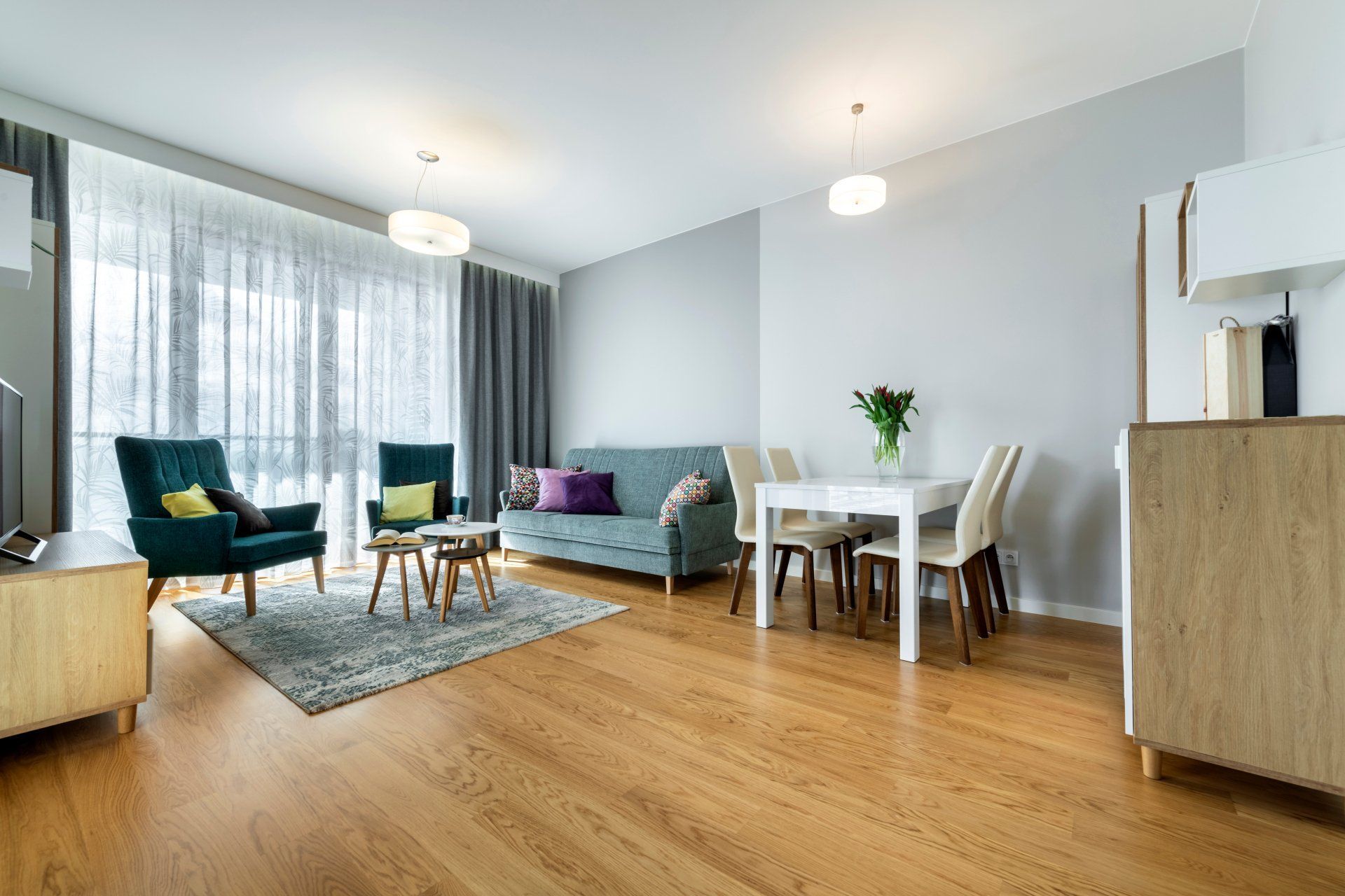 Salon moderne et lumineux avec chaises bleu canard, table à manger, canapé et parquet près de grandes fenêtres