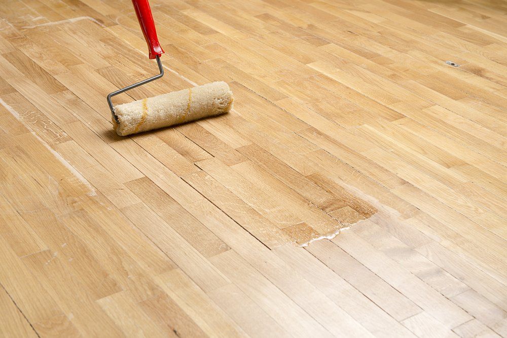 Une personne applique une finition sur un parquet à l'aide d'un rouleau à manche rouge