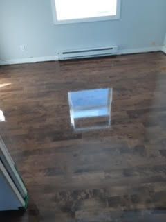 Pièce vide avec parquet foncé, murs blancs et une fenêtre se reflétant sur le sol.