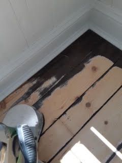 Plancher en bois peint, la peinture beige s'écaillant, et un embout d'aspirateur dans un coin.