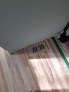 Sol du couloir imitation bois, grille d'aération murale et ruban adhésif vert près d'un cadre de porte