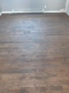 Pièce vide avec parquet foncé et un radiateur plinthe blanc le long du mur du fond.