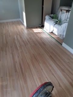 Pièce vide avec parquet clair et une tête d'aspirateur rouge et noire au premier plan.