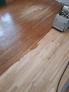Plancher en bois franc partiellement poncé, avec une ponceuse à plancher dans le coin supérieur droit