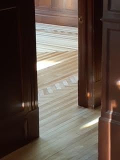 Une porte en bois s'ouvre sur un parquet baigné de soleil, où la lumière vive inonde l'espace.