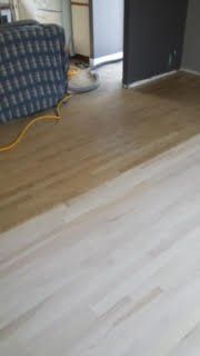 Plancher en bois clair partiellement installé, avec un canapé et une porte en arrière-plan.