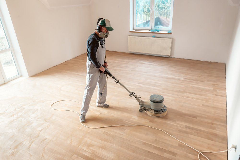 Une personne ponce un parquet avec une ponceuse à parquet dans une pièce lumineuse et vide.