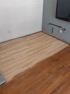 Parquet partiellement poncé dans une pièce aux murs blancs et avec une télévision fixée au mur de droite.