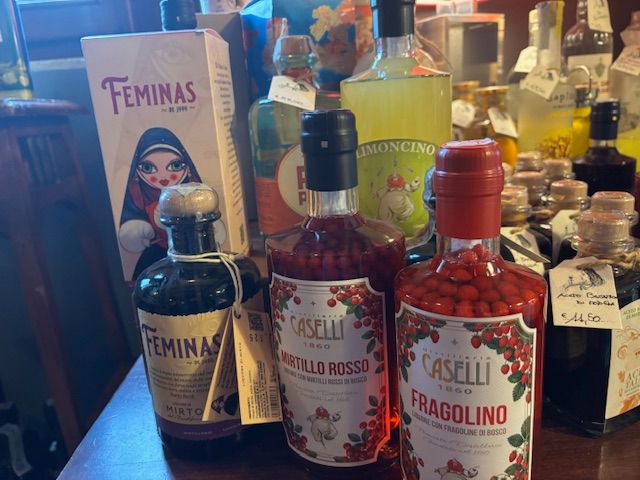 Diverse bottiglie di liquore su un bancone da bar, tra cui quelle delle marche Feminas, Rosso, Fragolino e Calo Vino Estremo Enoteca Soliera Apuana e La Spezia