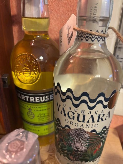 Due bottiglie di liquore, una di Chartreuse giallo-verde e una di Bacardi Aguardiente trasparente con etichetta bianca Vino Estremo Enoteca Soliera Apuana e La Spezia