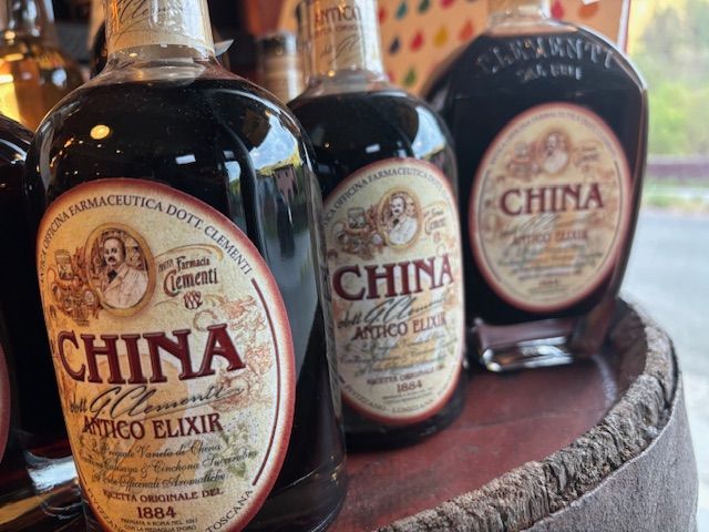 Tre bottiglie marroni di China Mico Elixir su un vassoio di legno, con le etichette rivolte in avanti Vino Estremo Enoteca Soliera Apuana e La Spezia