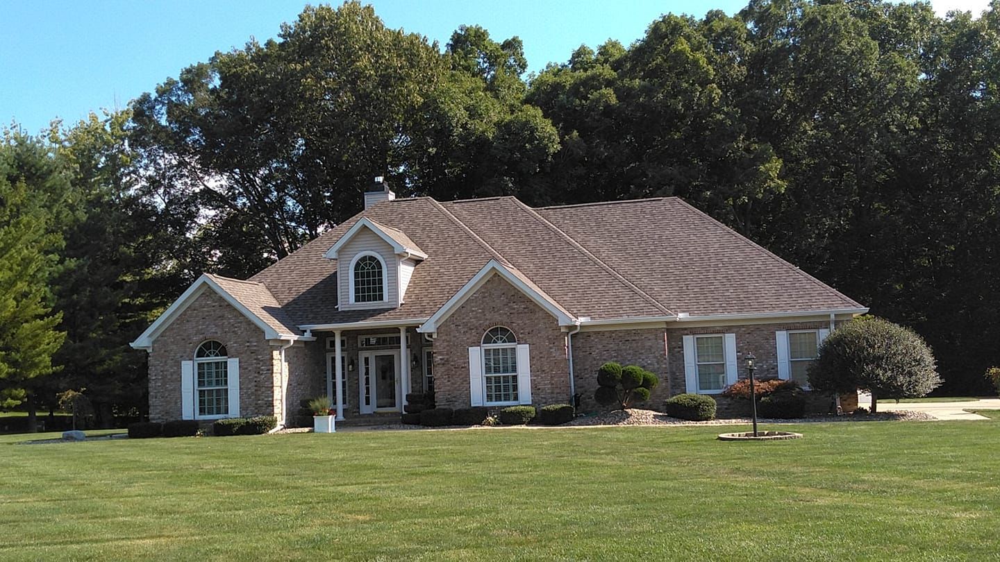 A large brick house sits in the middle of a lush green field