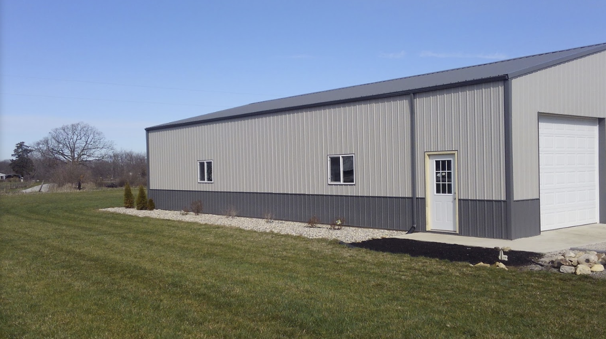 A large metal building with a garage door is sitting in the middle of a grassy field.