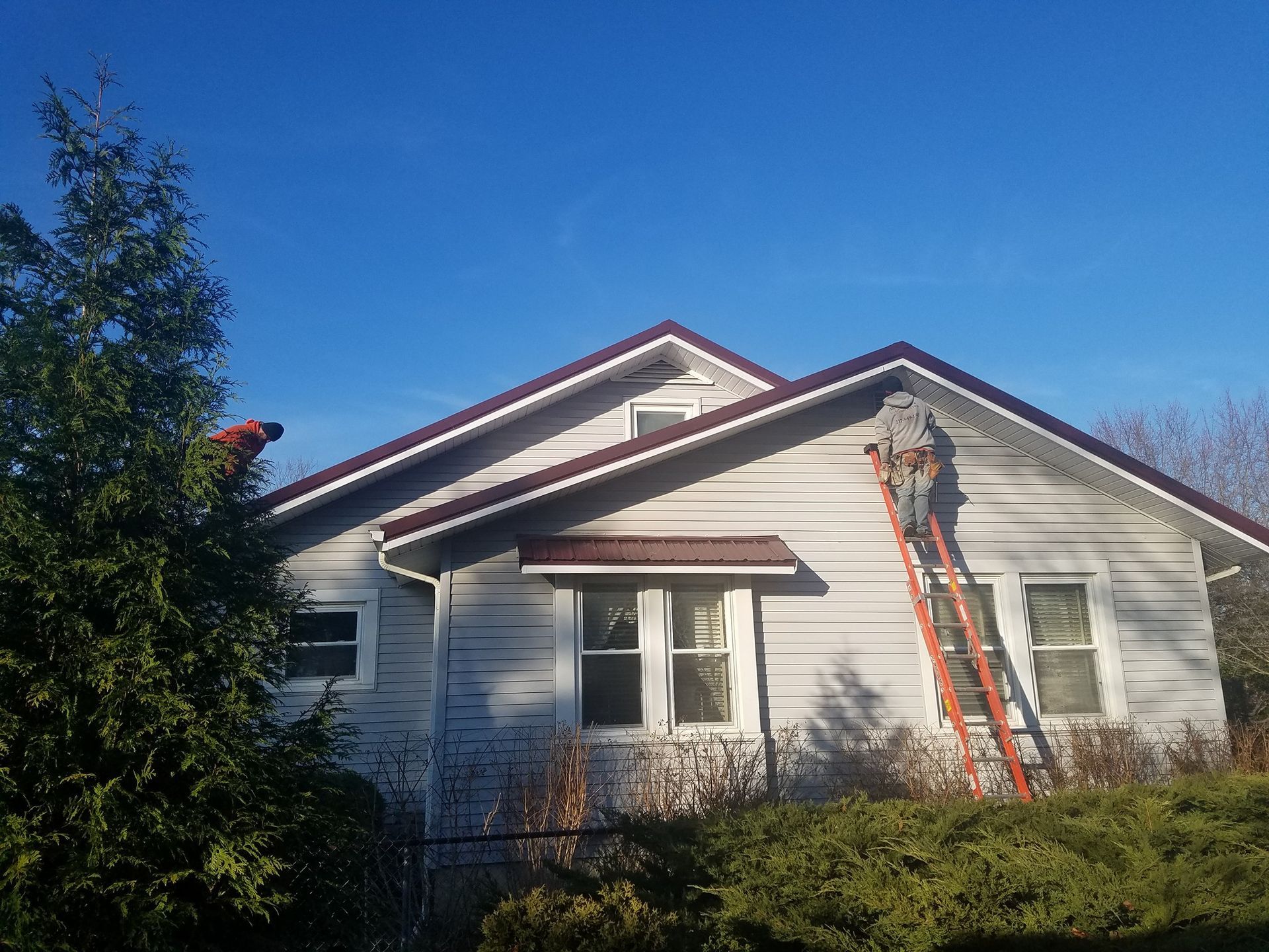 A man on a ladder is painting the roof of a house.