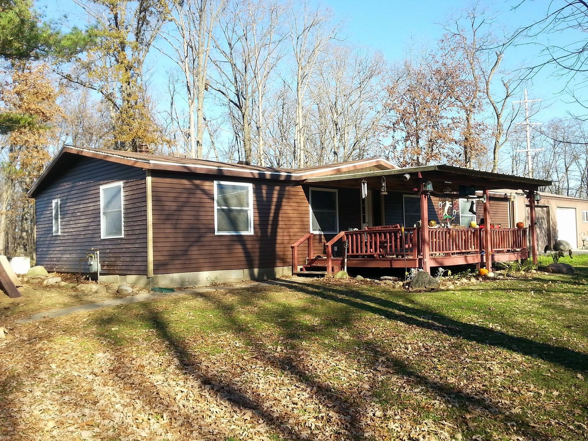 A brown mobile home with a red porch and trees in the background.