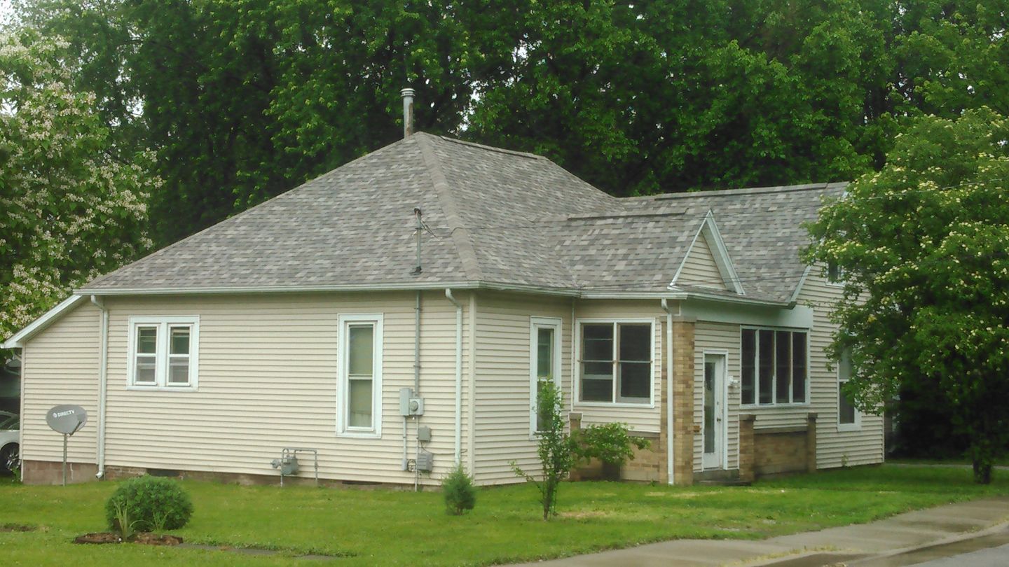 A white house with a gray roof is surrounded by trees