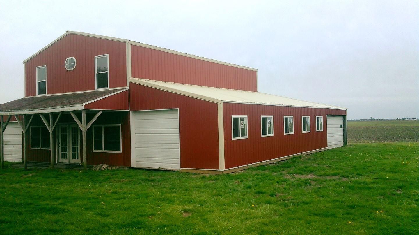 A red and white barn is sitting in the middle of a grassy field.