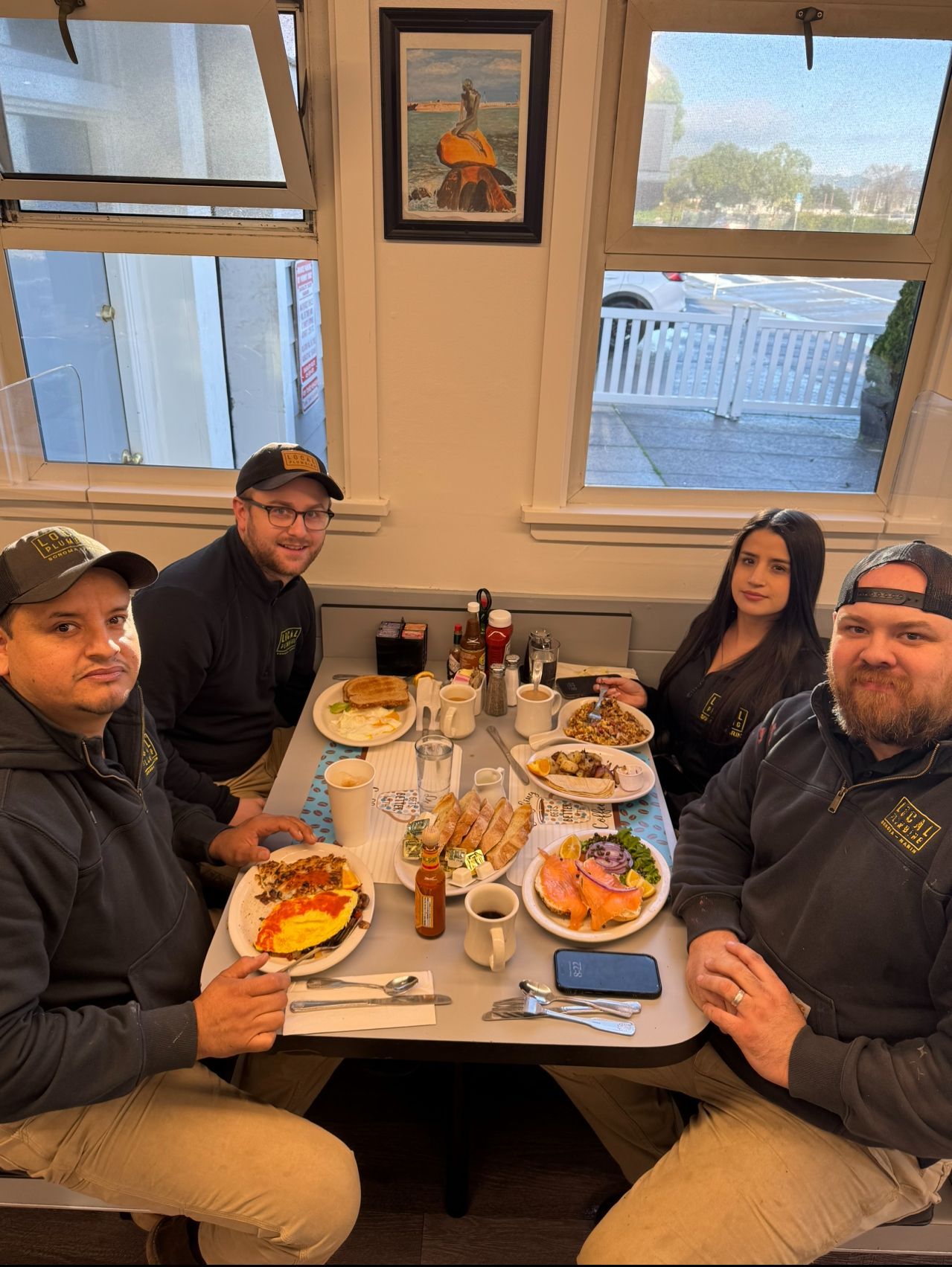 Four people seated around a table in a diner, eating breakfast. Sunlight streams in.