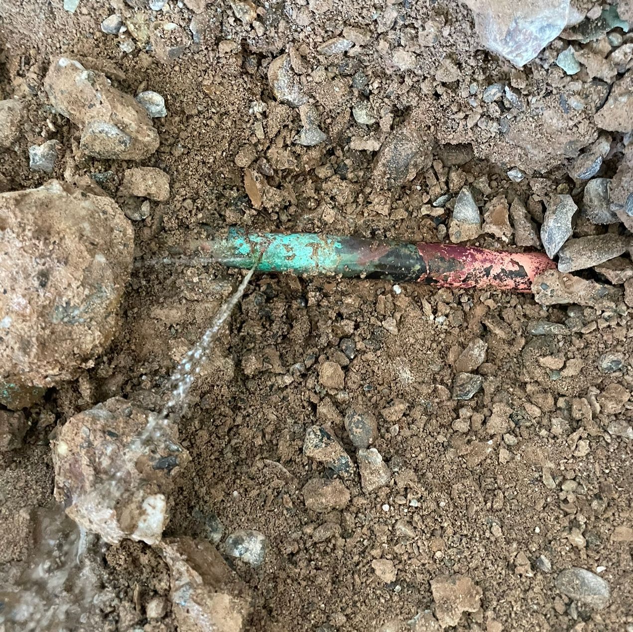 underground copper piping showing an obvious failure and water leaking from it