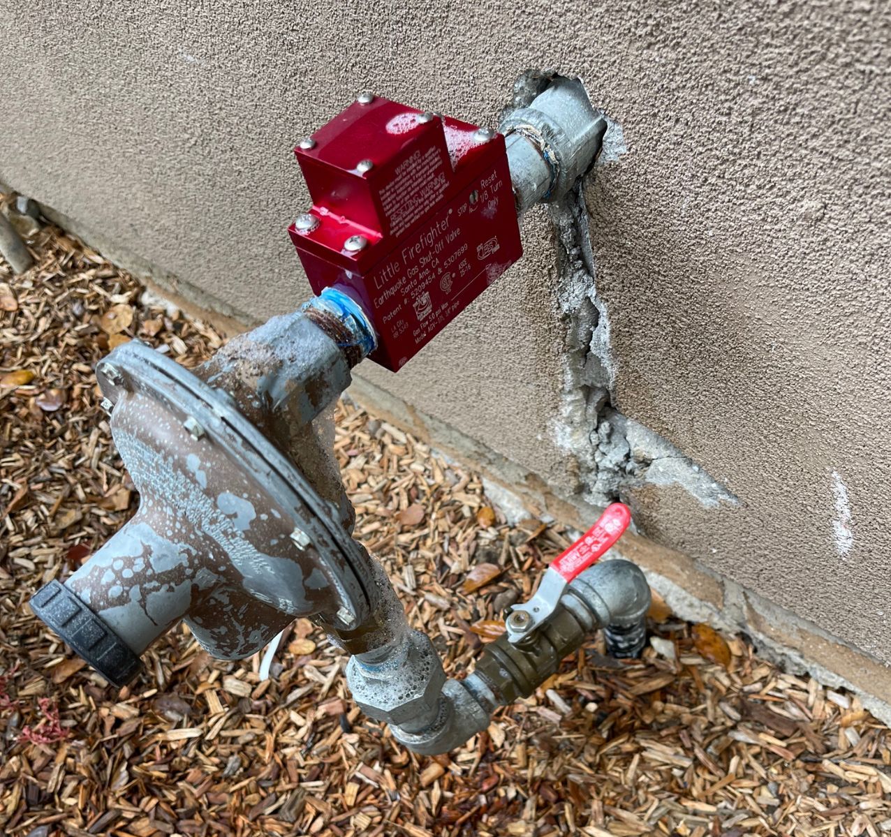 Red water valve connected to an old metal pipe, mounted to a stucco wall.