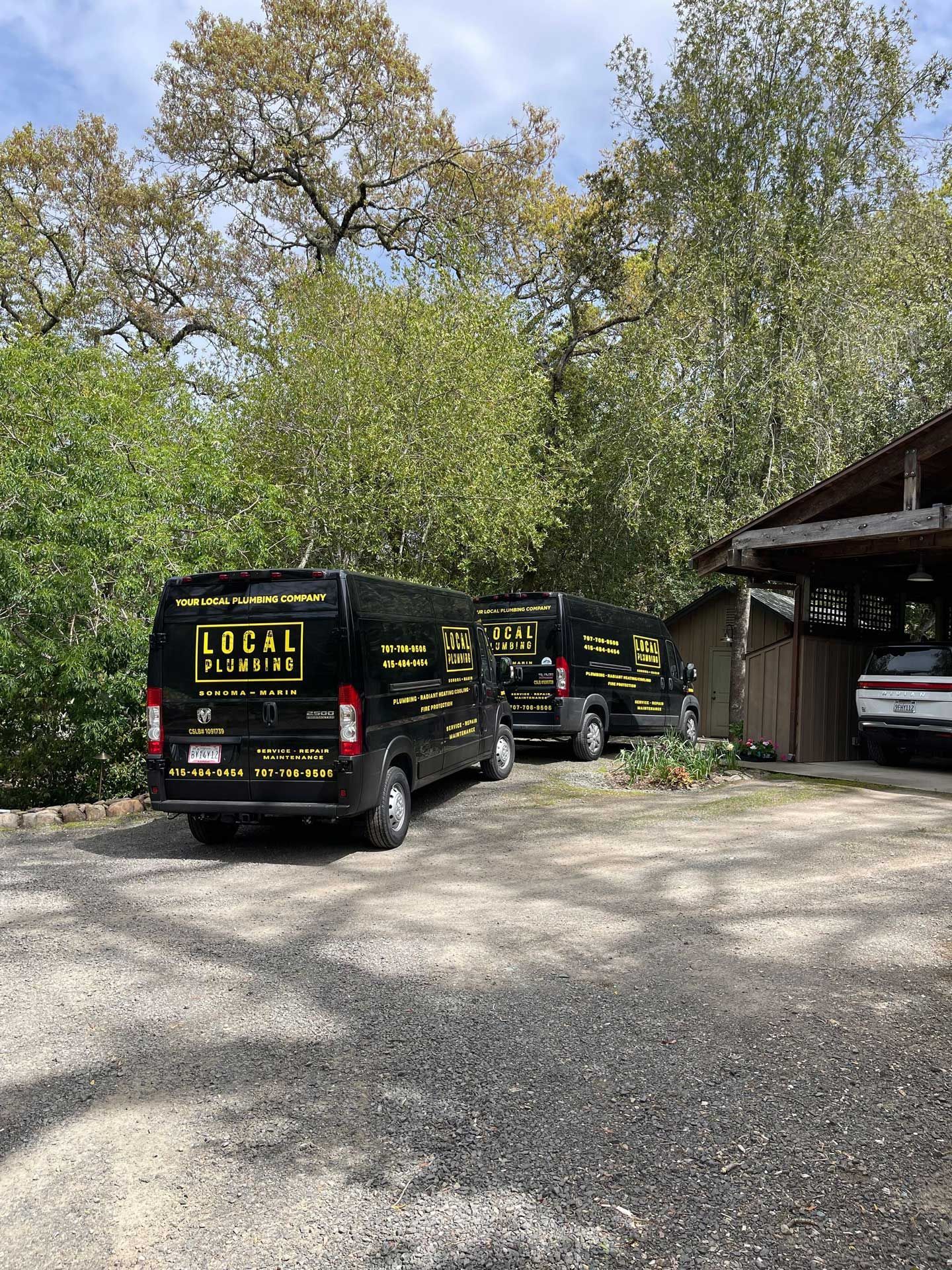 Two black vans with yellow text parked in front of a wooden building, trees in the background.